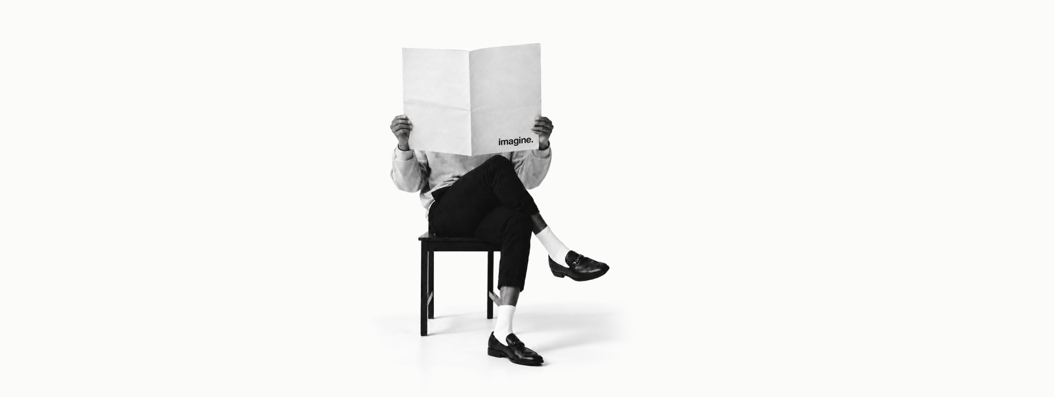 Person seated behind an open paper marked imagine